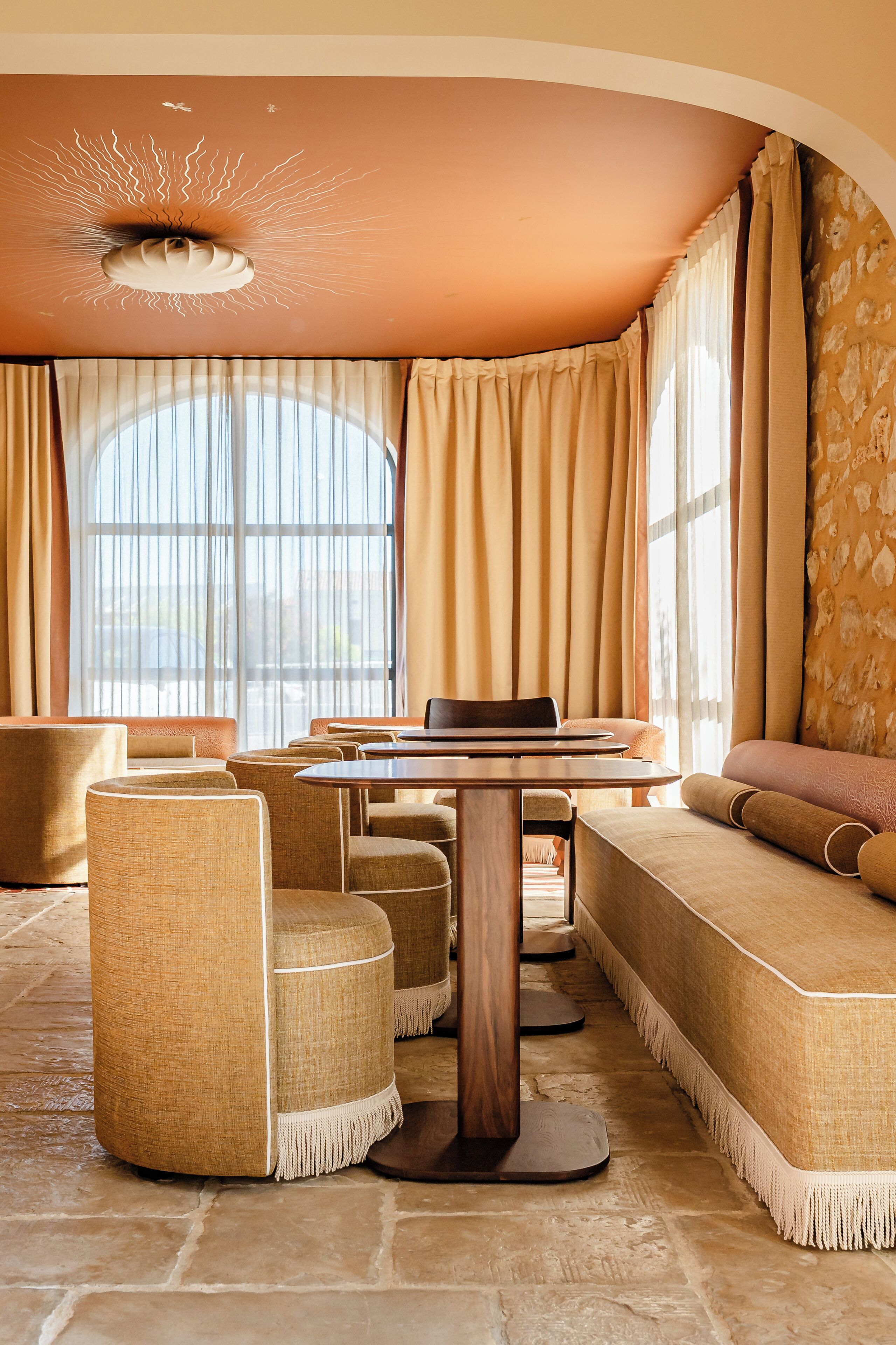 A room with a round table, cushioned seating, and a large window with curtains.