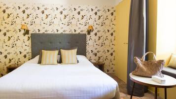 A hotel room with a bed, two wall-mounted lamps, a sofa, and a small table with a bag.