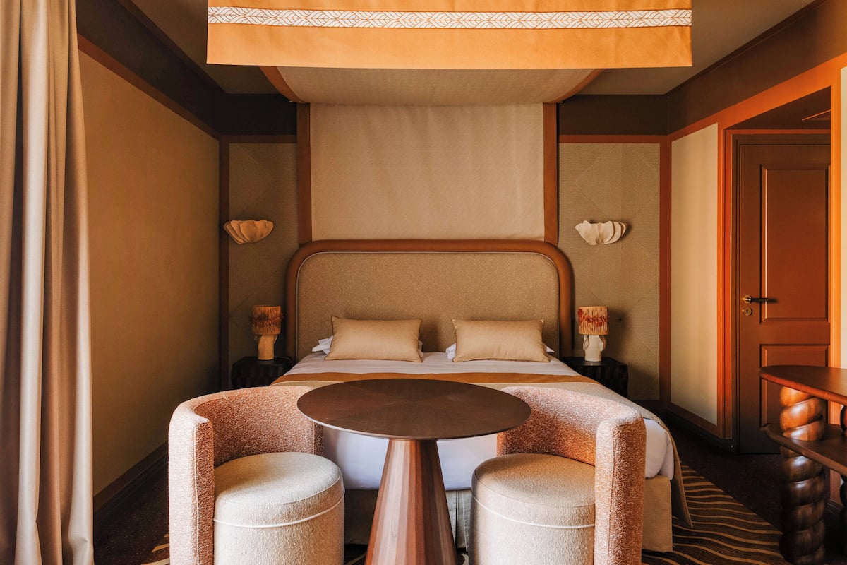 A hotel room with a bed, two bedside tables, a round table, two chairs, and a door.