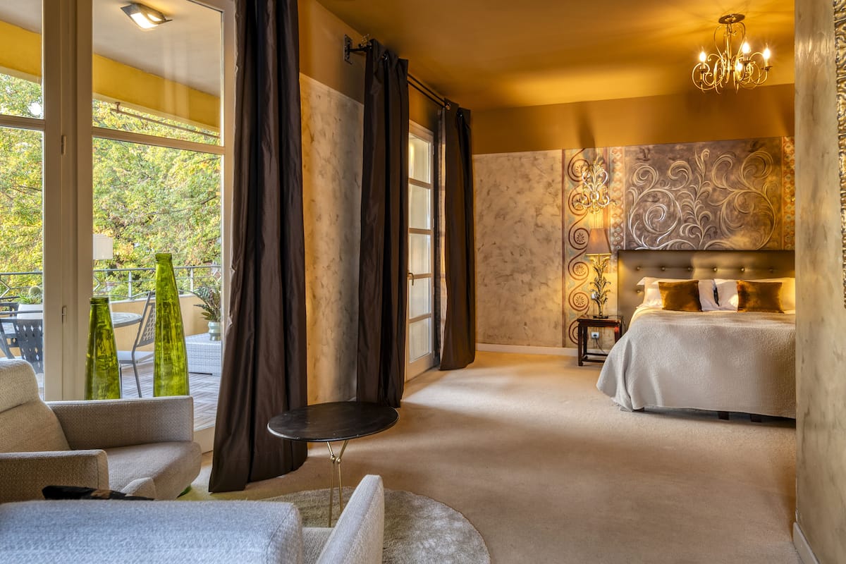 A bedroom with a bed, a nightstand, a chandelier, and a view of the outdoors.