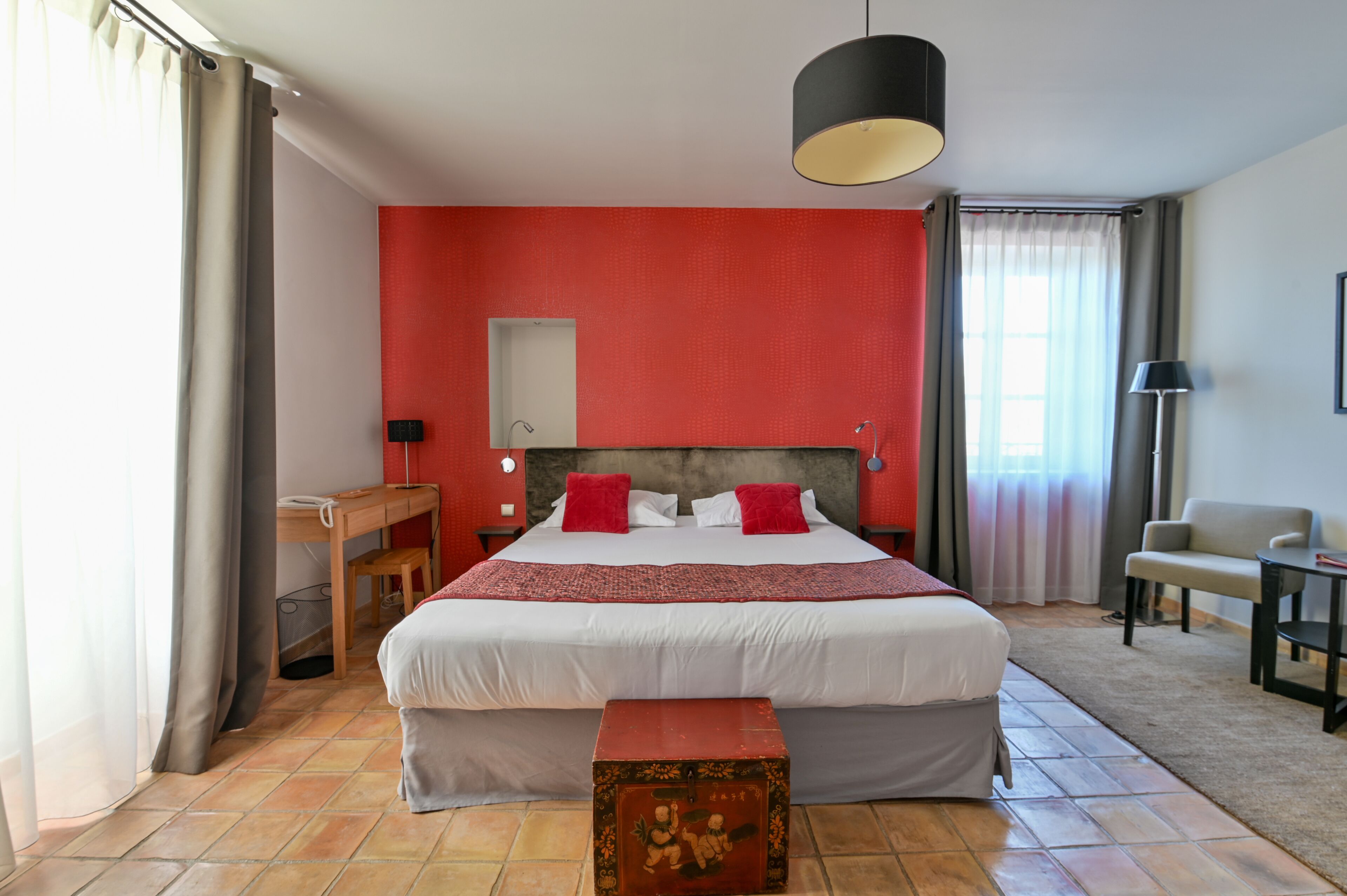 A hotel room with a large bed, a desk, a chair, and a small table.
