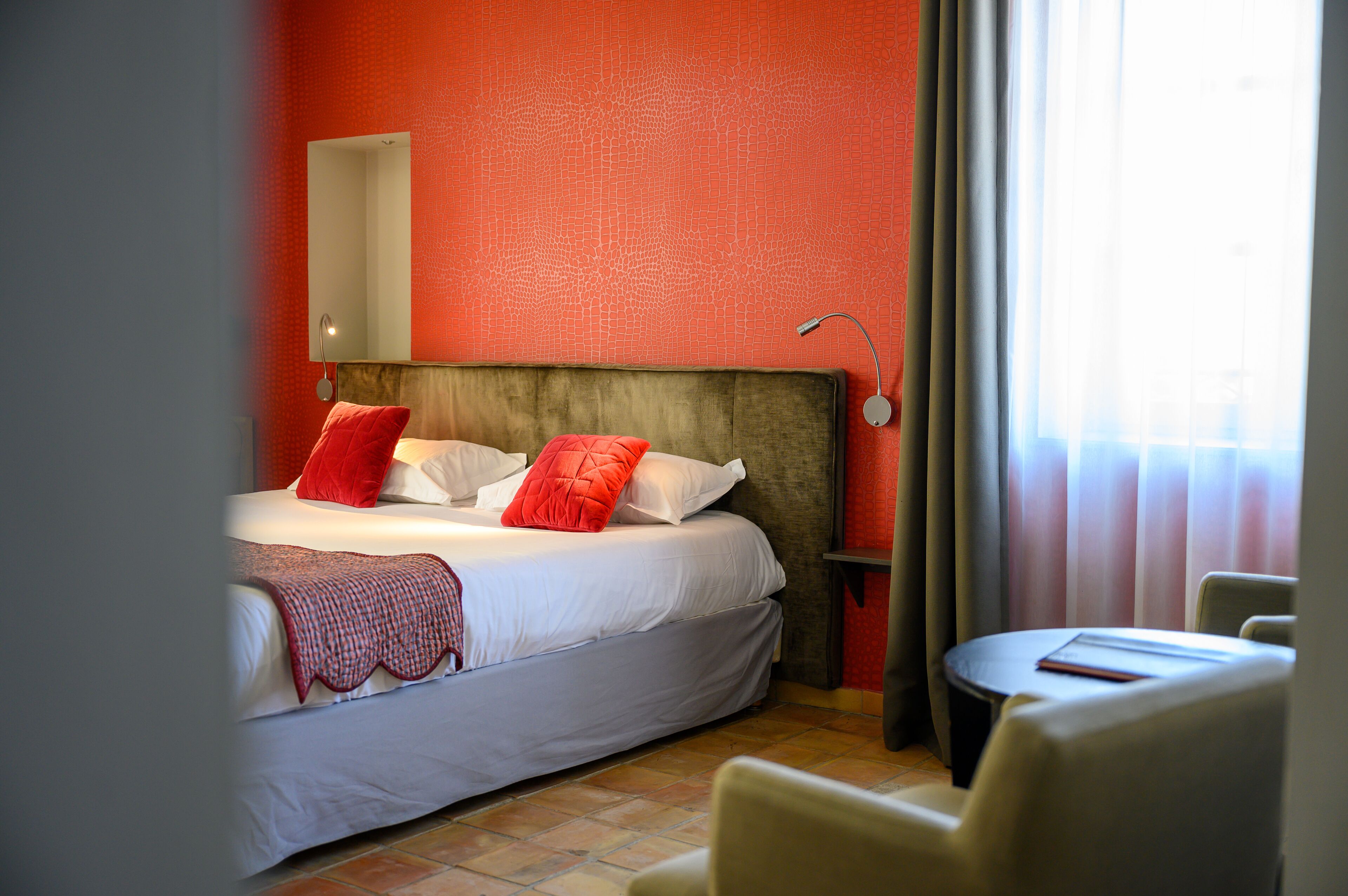 Ein Hotelzimmer mit Bett, Nachttisch, Stuhl und einem Fenster mit Vorhängen.