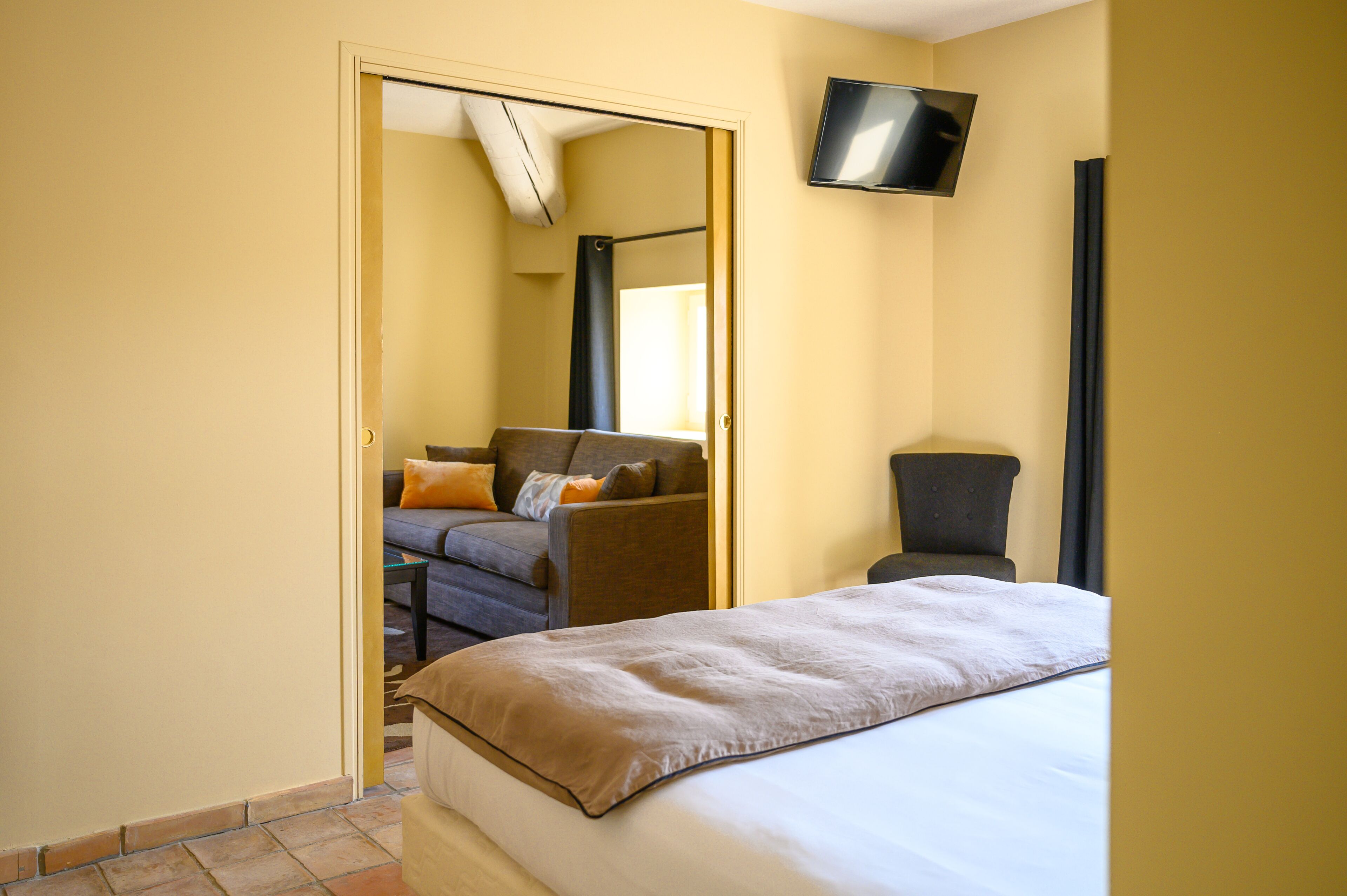 Ein Hotelzimmer mit Bett, Sofa, Sessel, Fernseher und einem durchgegangenen Tür erkennbaren Badezimmer.