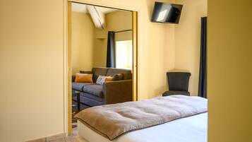 Ein Hotelzimmer mit Bett, Sofa, Sessel, Fernseher und einem durchgegangenen Tür erkennbaren Badezimmer.