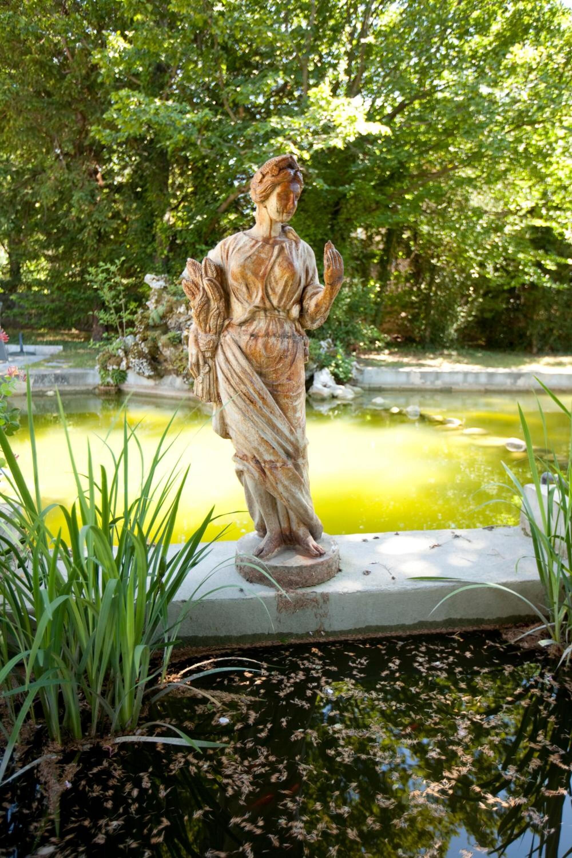 A statue of a woman in a garden with a pond and greenery.