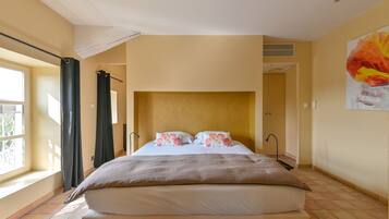 Un dormitorio con una cama grande, una ventana con cortinas, un cuadro en la pared y una puerta que da a otra habitación.