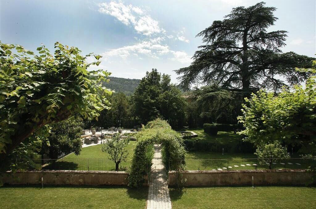 A pathway leading through a park with a large tree and a view of a cemetery in the distance.