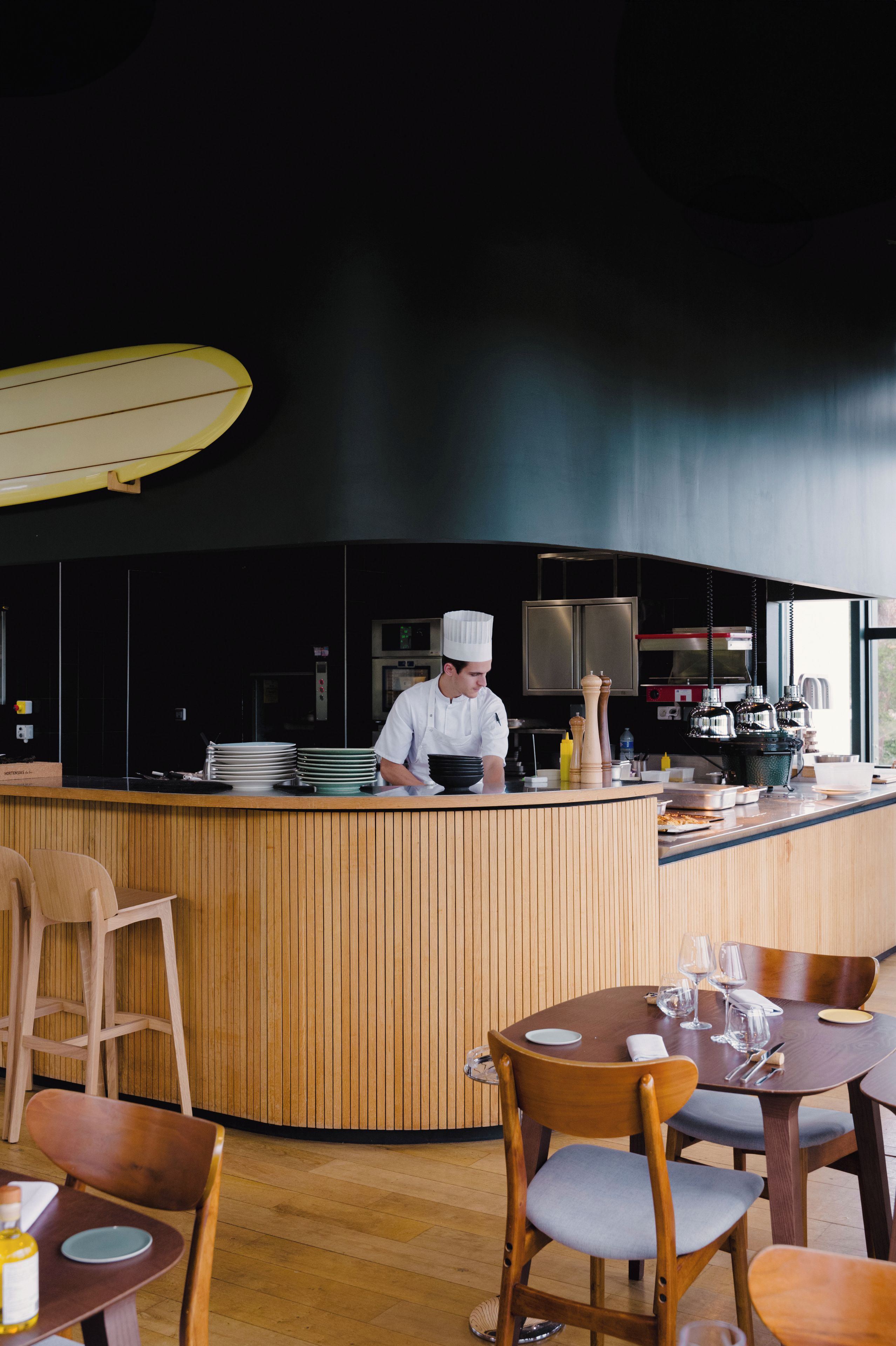 Interior moderno de restaurante con un chef en la barra, paneles de madera y zona de bar.