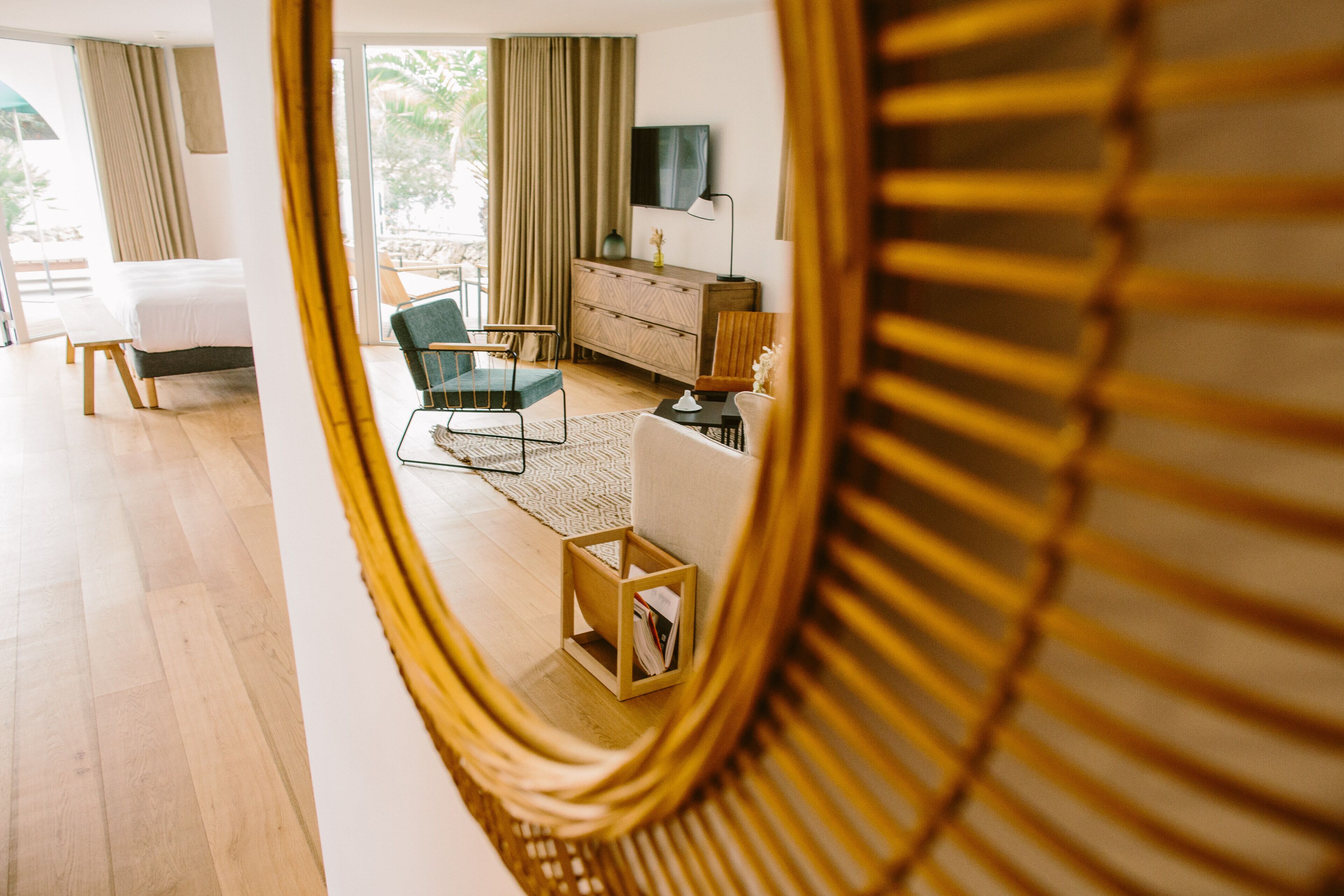 Une chambre d’hôtel moderne avec un grand lit, un coin salon comprenant un canapé et des fauteuils, une commode en bois et un téléviseur fixé au mur.
