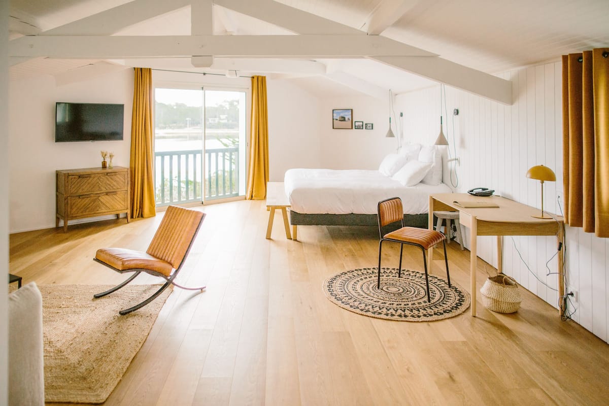 Ein Schlafzimmer mit Bett, Schreibtisch, Stuhl, Fernseher und Blick ins Freie.