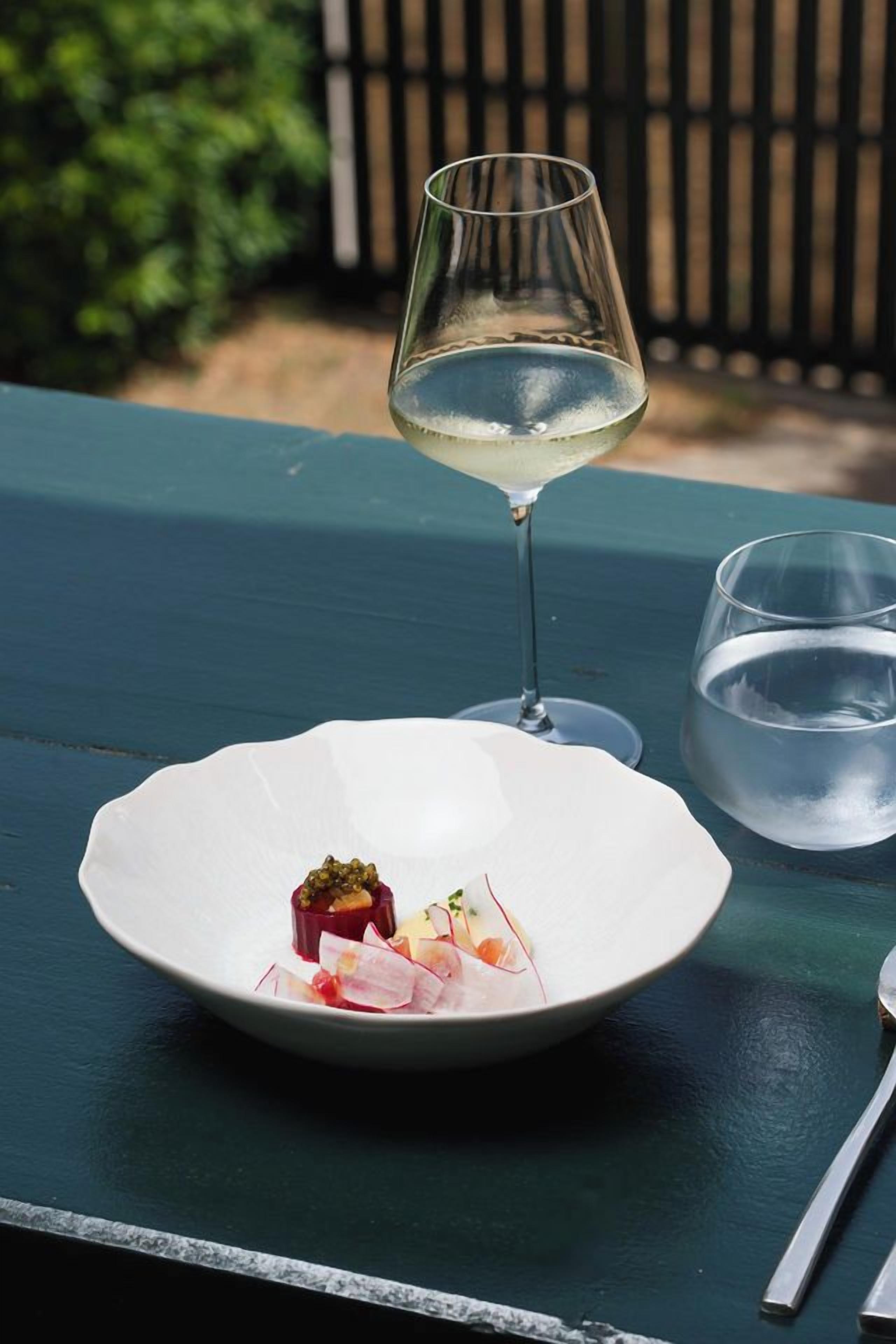 Ein Esstisch mit einer Speiseplatte, einem Glas Weißwein und einem Glas Wasser.