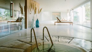 Un espace intérieur spacieux avec un mur de verre, un coin salon avec un banc et un vase décoratif contenant des plumes d’herbe des pampas.
