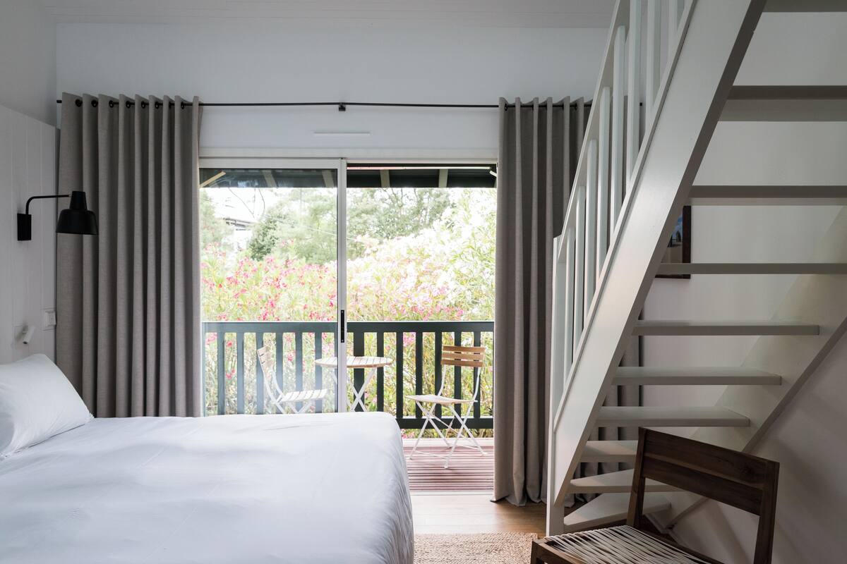Ein Schlafzimmer mit Bett, einem Balkon mit Tisch und Stühlen sowie einer Treppe.