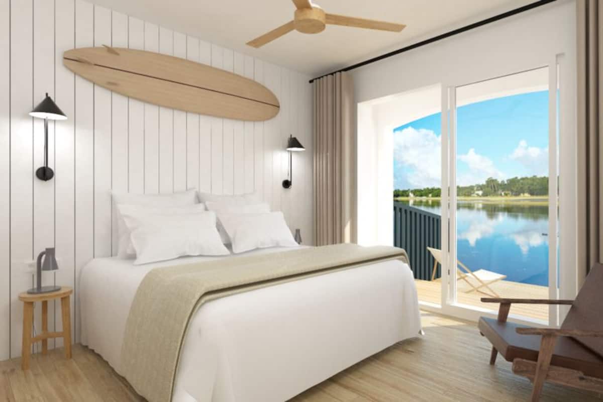 Ein Schlafzimmer mit einem Bett, Nachttischlampen, einem Deckenventilator und Blick auf einen See durch eine Schiebetür.