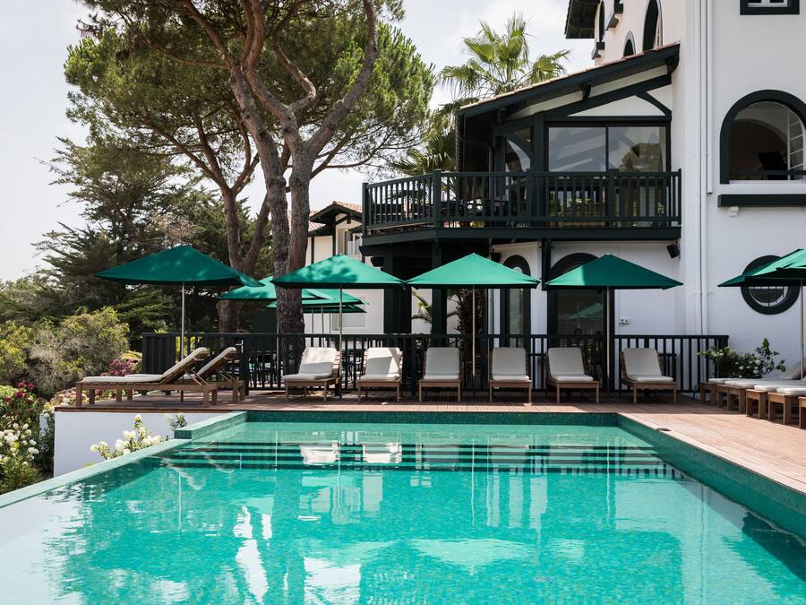 A pool area with lounge chairs and umbrellas, surrounded by a white building with balconies.