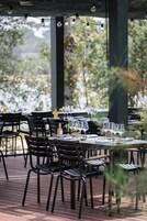 An outdoor dining area with tables and chairs, a bottle of wine, and a view of trees.