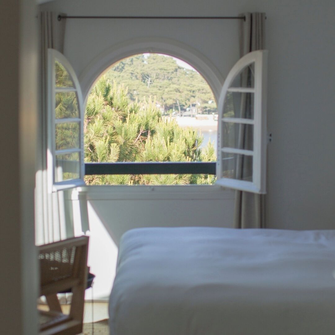 A bedroom with a large arched window overlooking a beach and greenery.