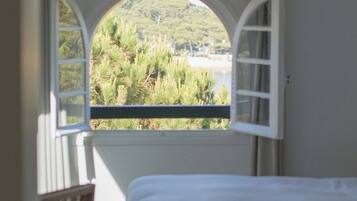 A bedroom with a large arched window overlooking a beach and greenery.