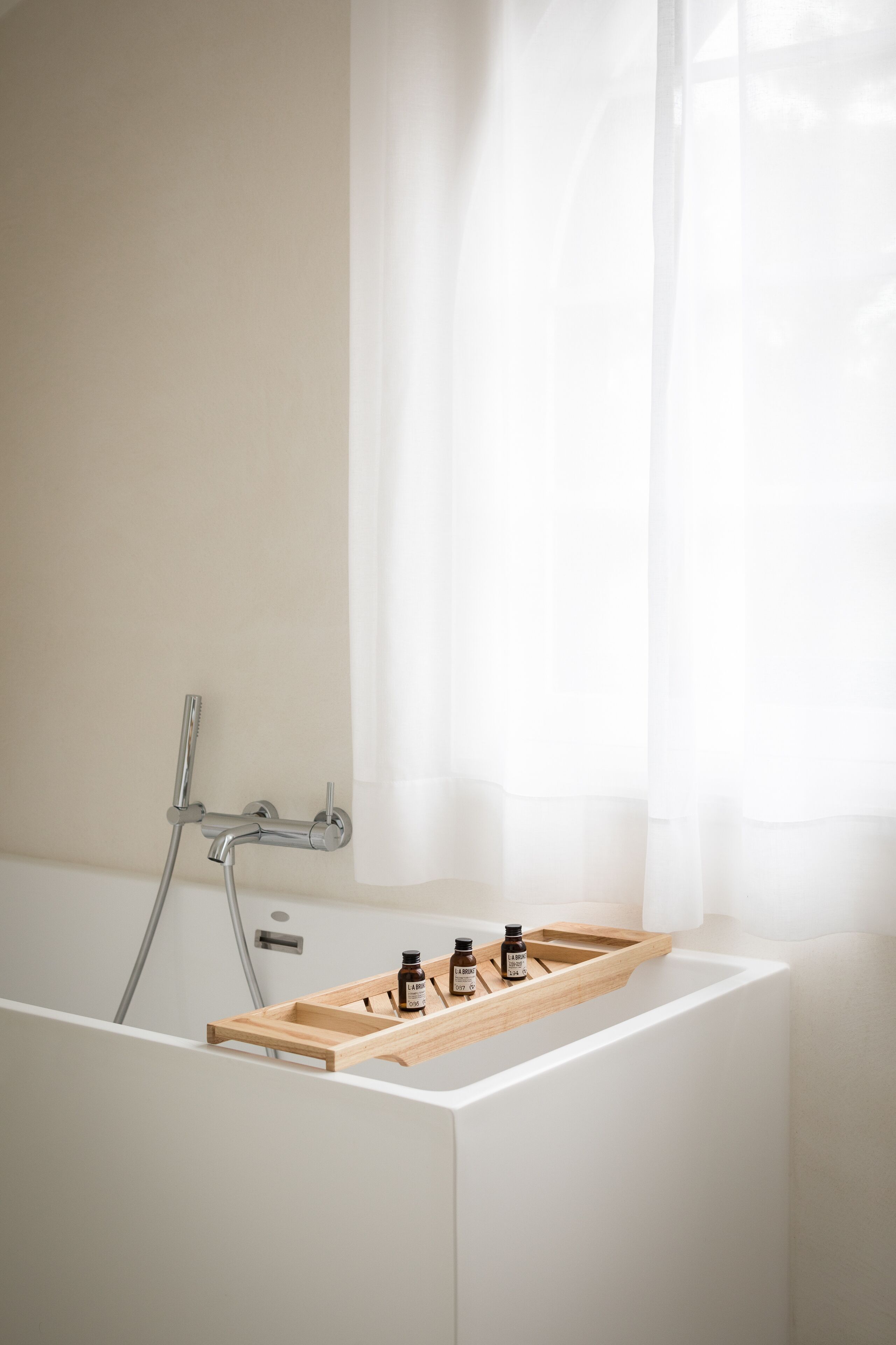 A modern bathroom with a bathtub, a wooden tray with bottles, and a showerhead.