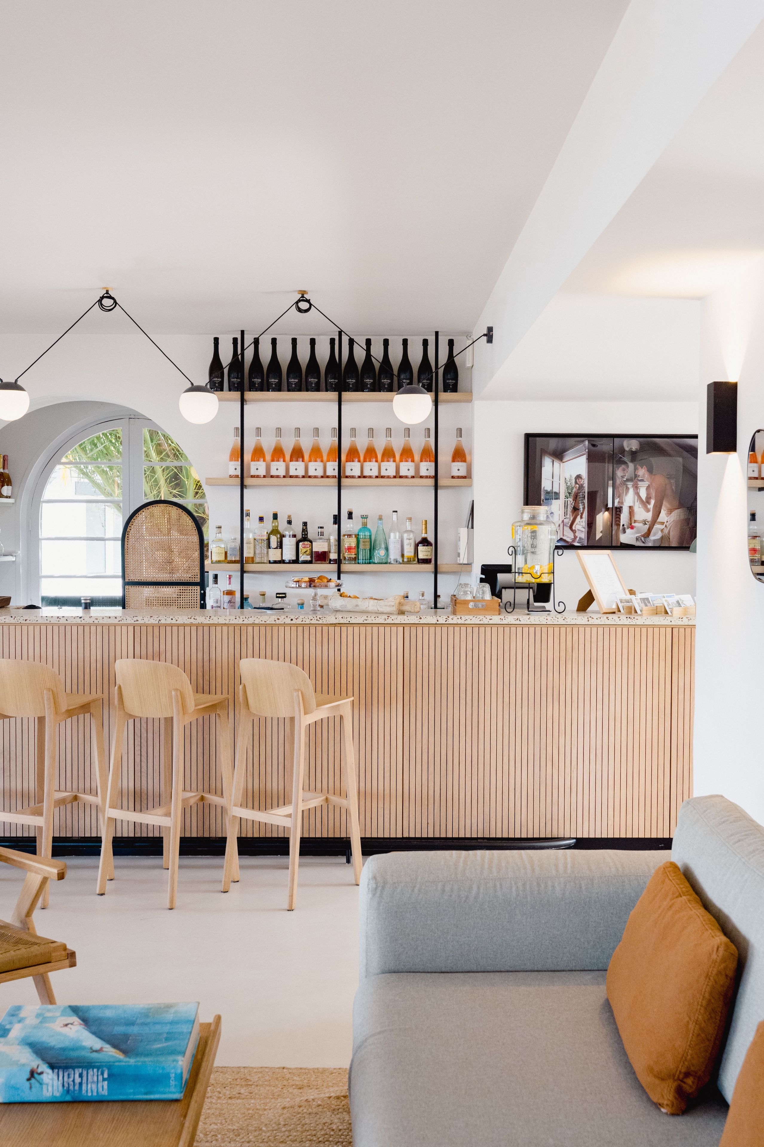 A modern bar area with wooden bar counter, hanging pendant lights, and a seating area with wooden chairs.
