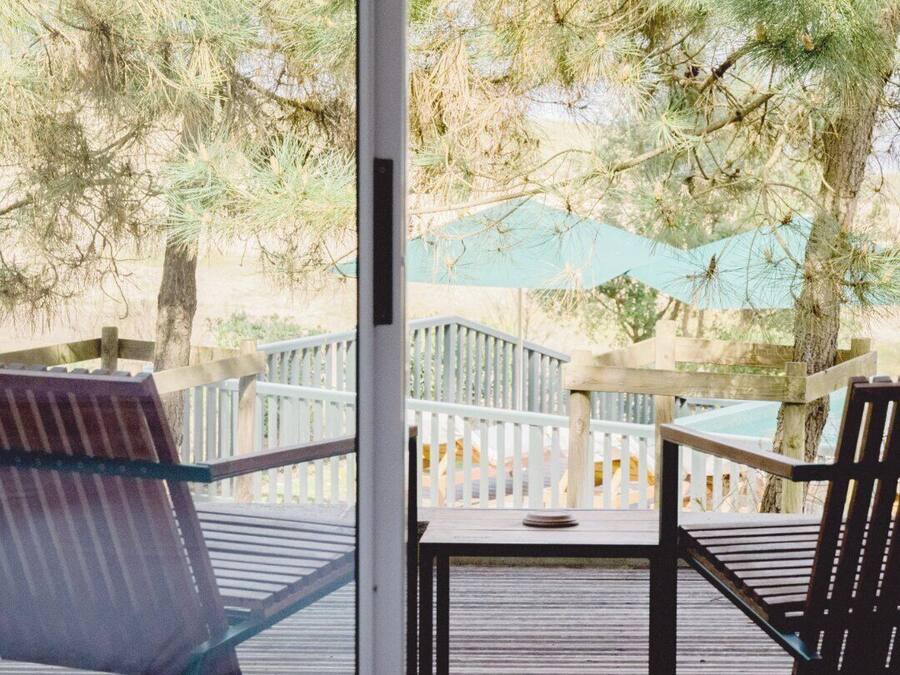 A deck with two chairs and a table, overlooking a pool and trees.