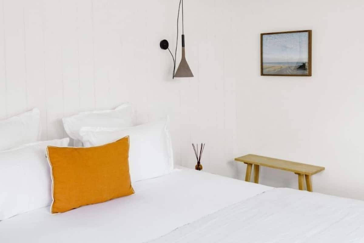 Ein Schlafzimmer mit einem Bett, einem Nachttisch, einer Pendelleuchte und einem gerahmten Bild an der Wand.