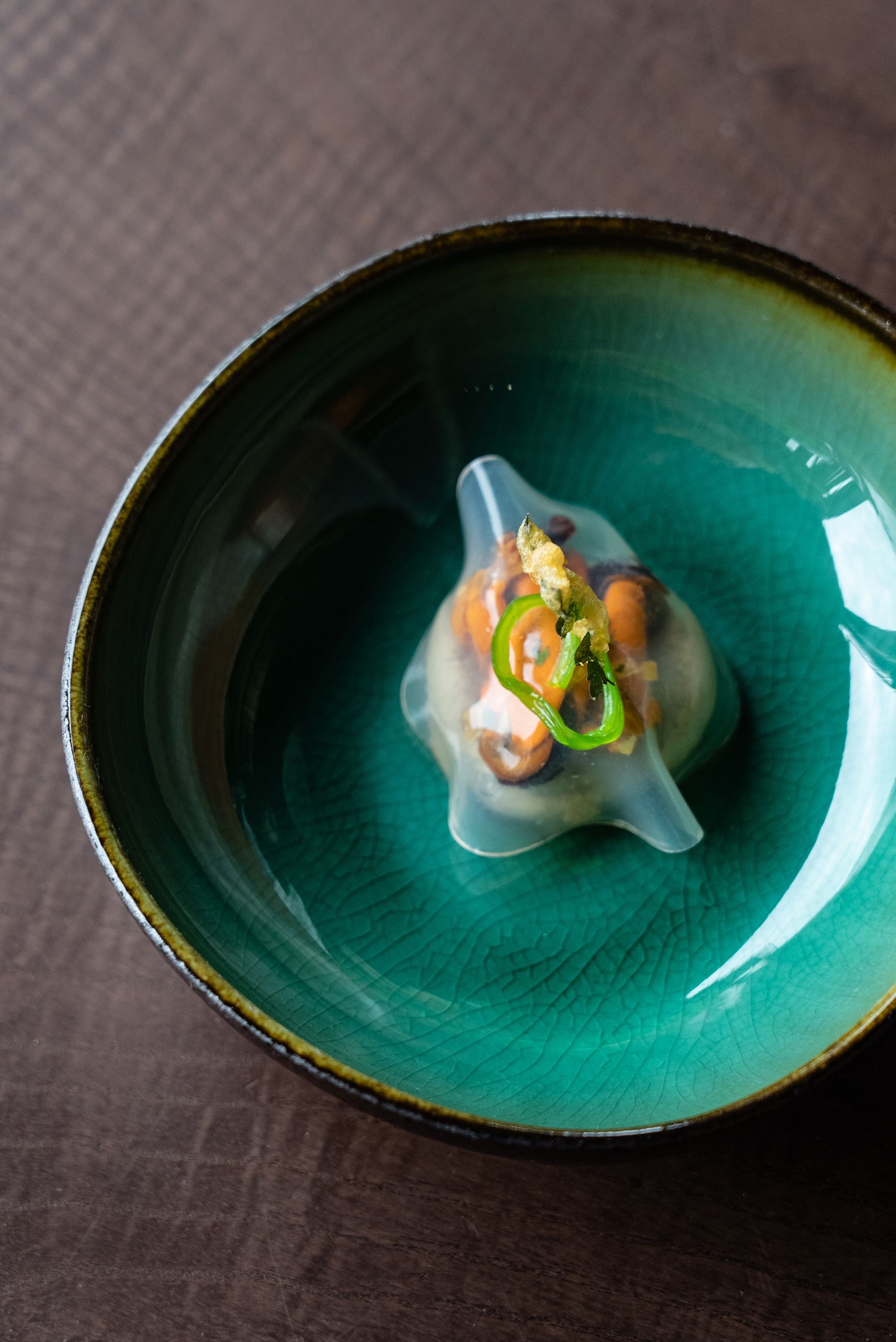 A ceramic bowl with a green glaze and a dark interior, containing a food item with a garnish.