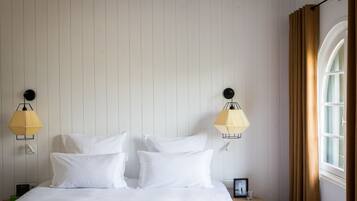 Un dormitorio con cama, dos lámparas de pared, una mesita pequeña y un ventanal con cortinas.