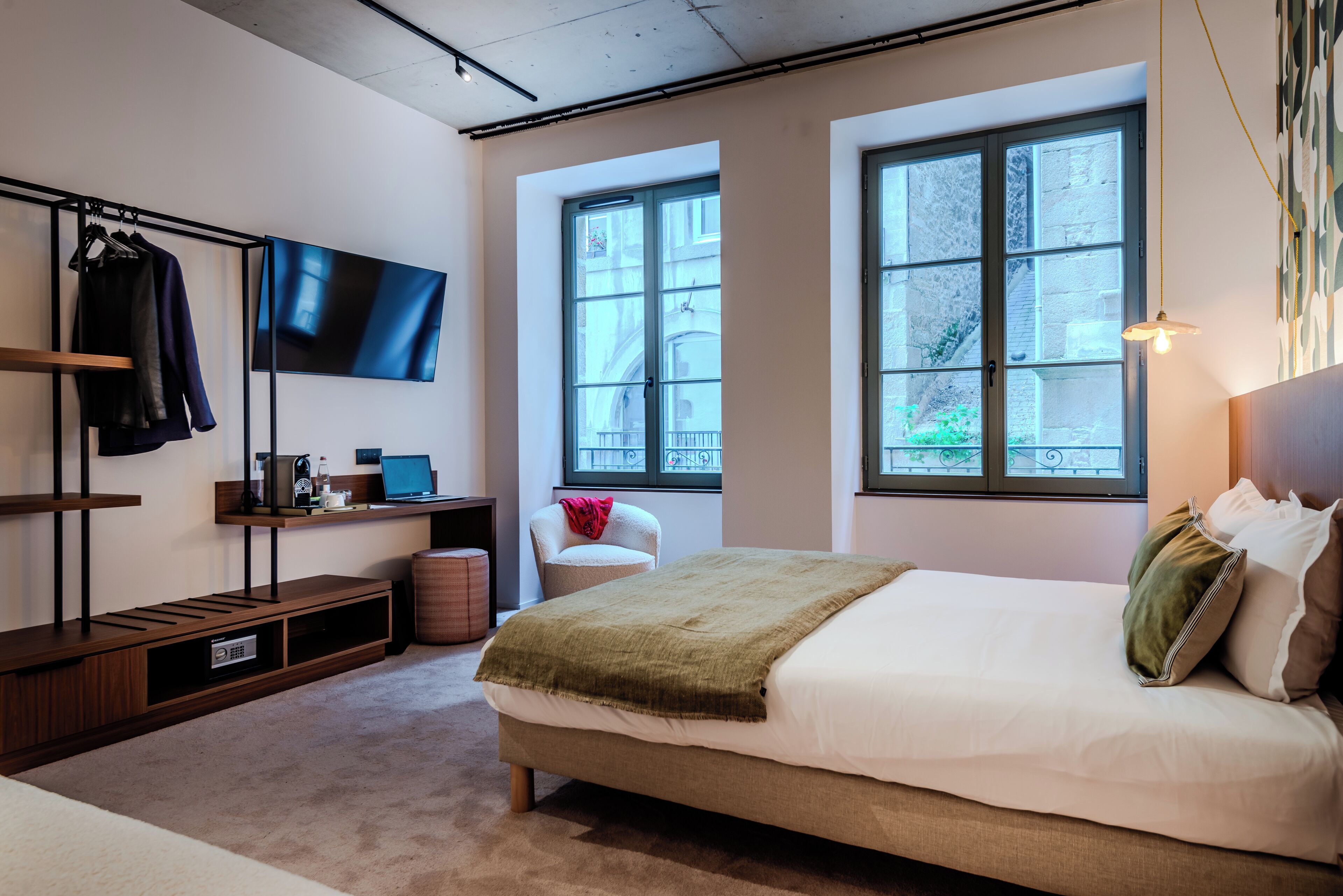 A modern bedroom with a large bed, a TV mounted on the wall, and a window providing a view of the outside.
