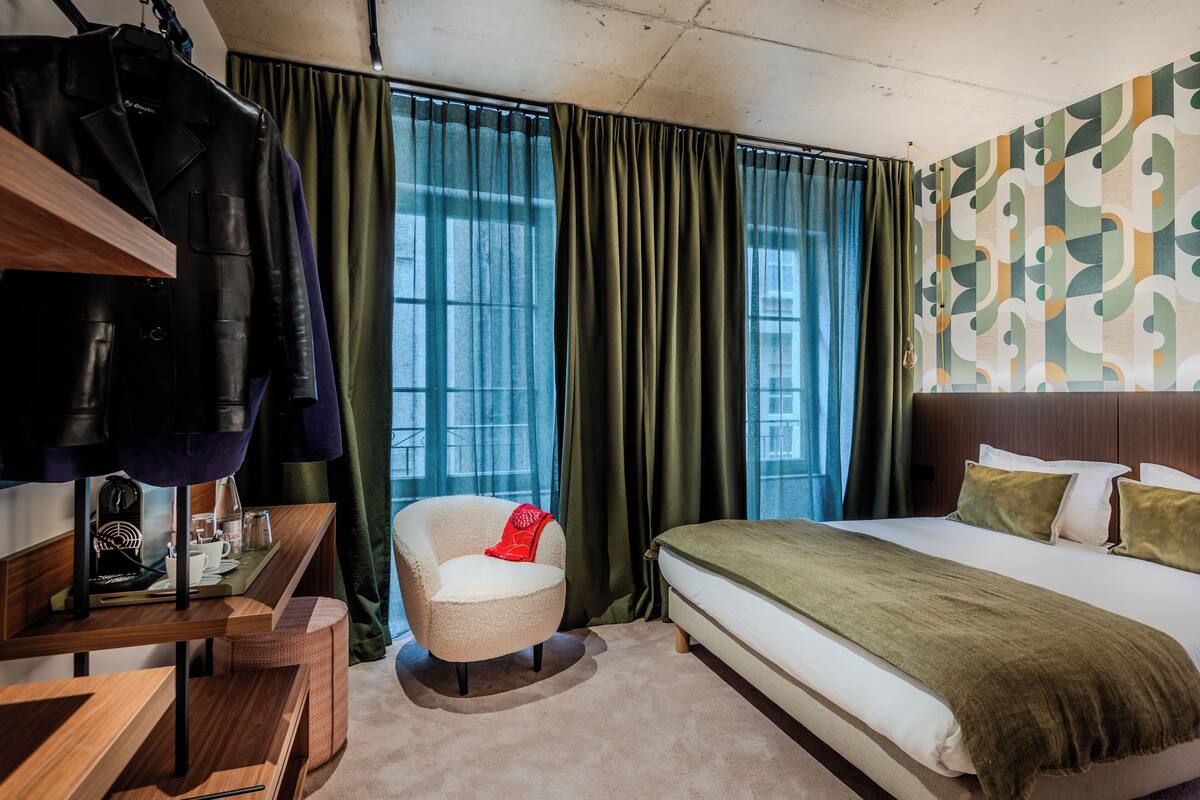A hotel room with a bed, a chair, a desk, and a coat rack.
