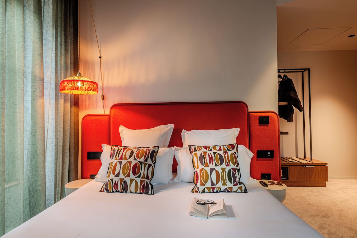 A hotel room with a red headboard, white bedding, and patterned pillows.