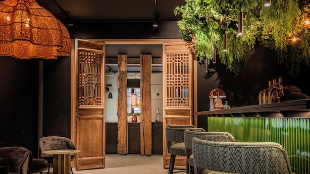 Een bar met houten meubels, een zithoek met groene kussens en een decoratieve hangplant.