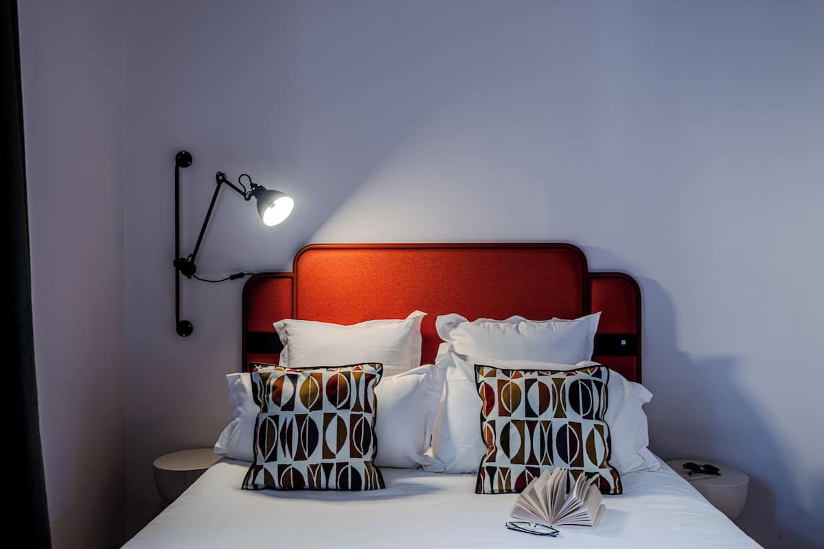 A neatly made bed with patterned pillows, a bedside lamp, and a book on the nightstand.