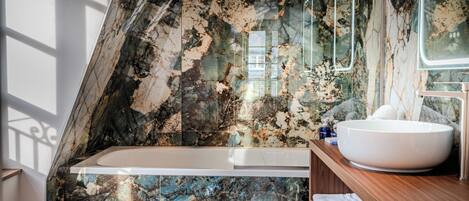 Un baño con pared de mármol, una bañera, un tocador de madera y un espejo grande.