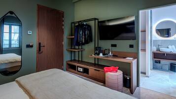 Une chambre d’hôtel avec un lit, une télévision, un bureau en bois, un miroir et une salle de bain visible à travers une porte ouverte.