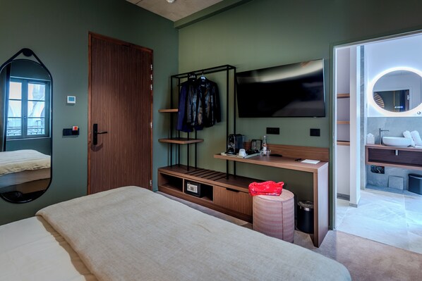 A hotel room with a bed, a TV, a wooden desk, a mirror, and a bathroom visible through an open door. - Hôtel Anne de Bretagne (Saint-Malo)