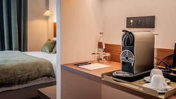 A hotel room with a bed, a small kitchenette with a coffee maker, a bottle of water, and a cup.