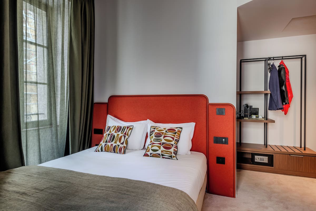 A hotel room with a bed, a bedside table, a wardrobe, and a window with curtains.