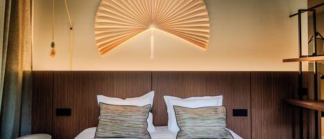 A modern hotel room with a large bed, two pillows, a wall-mounted fan, and a bedside table.