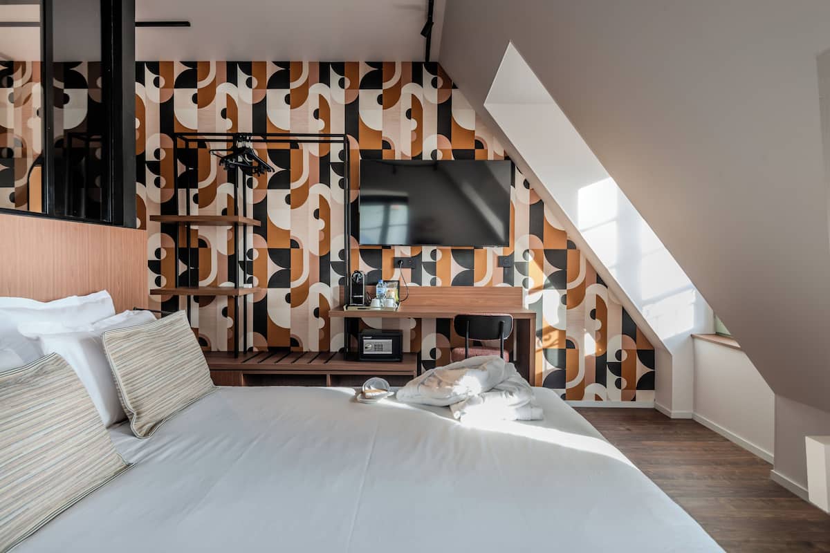 A modern hotel room with a bed, a desk, a TV, and a patterned wall.