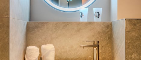 Un baño moderno con un espejo redondo, un lavabo blanco y una encimera de madera.