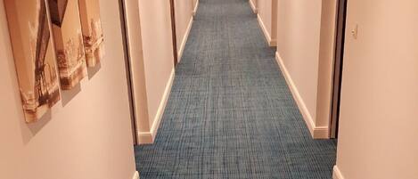 Un pasillo de hotel con alfombra azul, paredes blancas y puertas a ambos lados.
