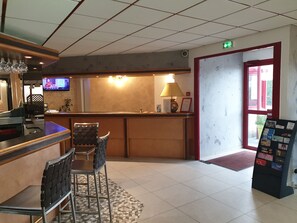 A reception area with a counter, chairs, a television, and a red door leading outside. - Hôtel Eclipse (Magnanville)