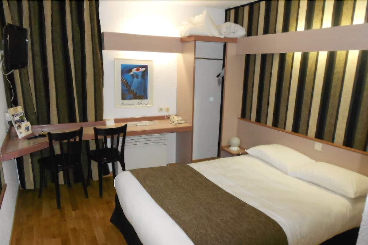 Un dormitorio con una cama, un escritorio, dos sillas, una mesita de noche pequeña, un teléfono en la pared y un cartel en la pared.