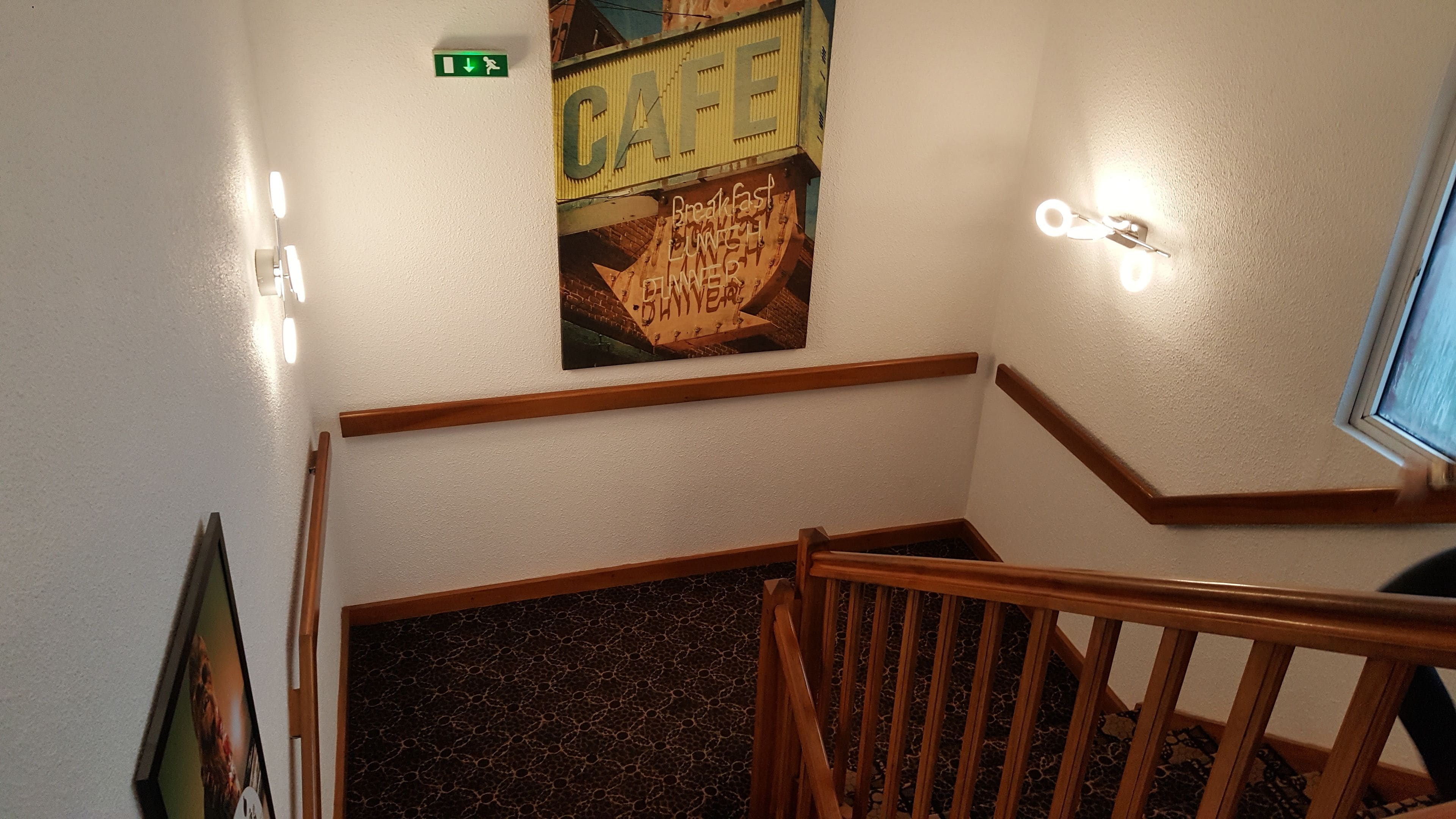 A staircase with wooden railings and a wall-mounted sign that reads "CAFE" with a poster below advertising breakfast, lunch, and dinner.