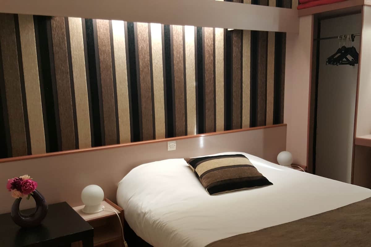 Una habitación de hotel con cama, mesitas de noche, lámpara, cómoda y espejo.