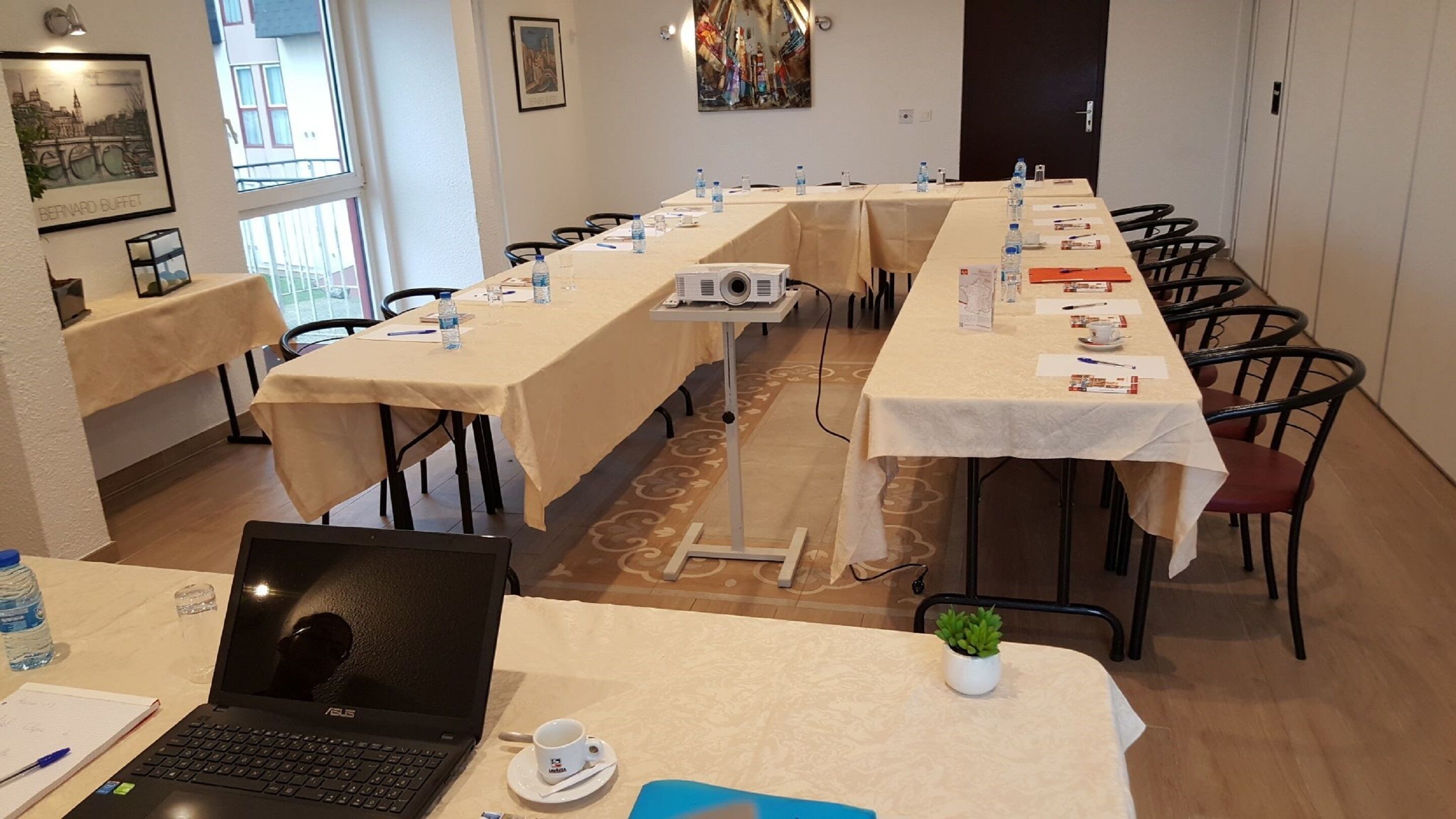 Kokoushuone, jossa on pitkiä pöytiä, kannettavia tietokoneita ja vesipulloja.