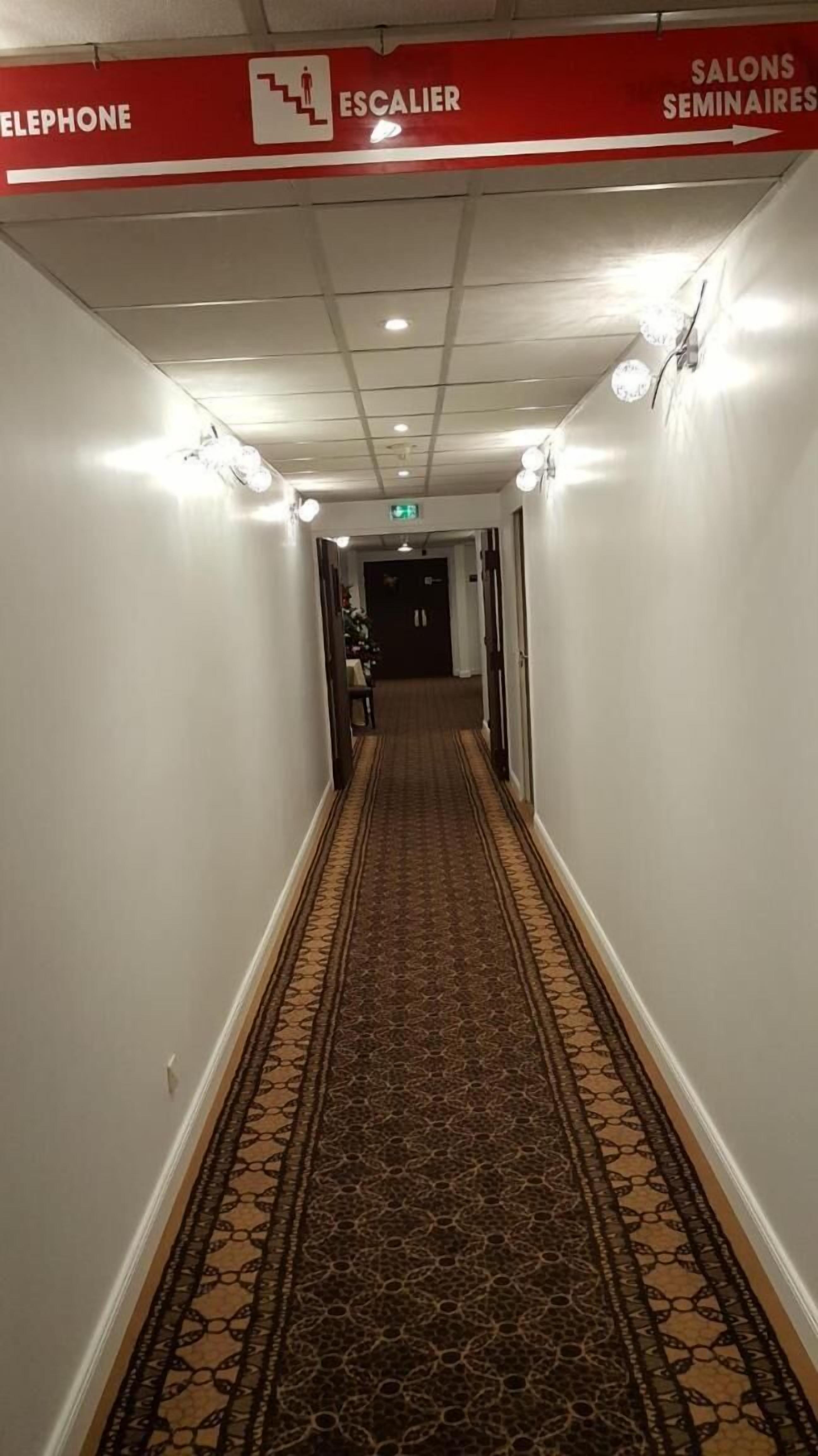 Een hotelgang met een kamerbreed tapijt, bewegwijzering naar de telefoon, roltrap en seminarruimtes, en inbouwverlichting.