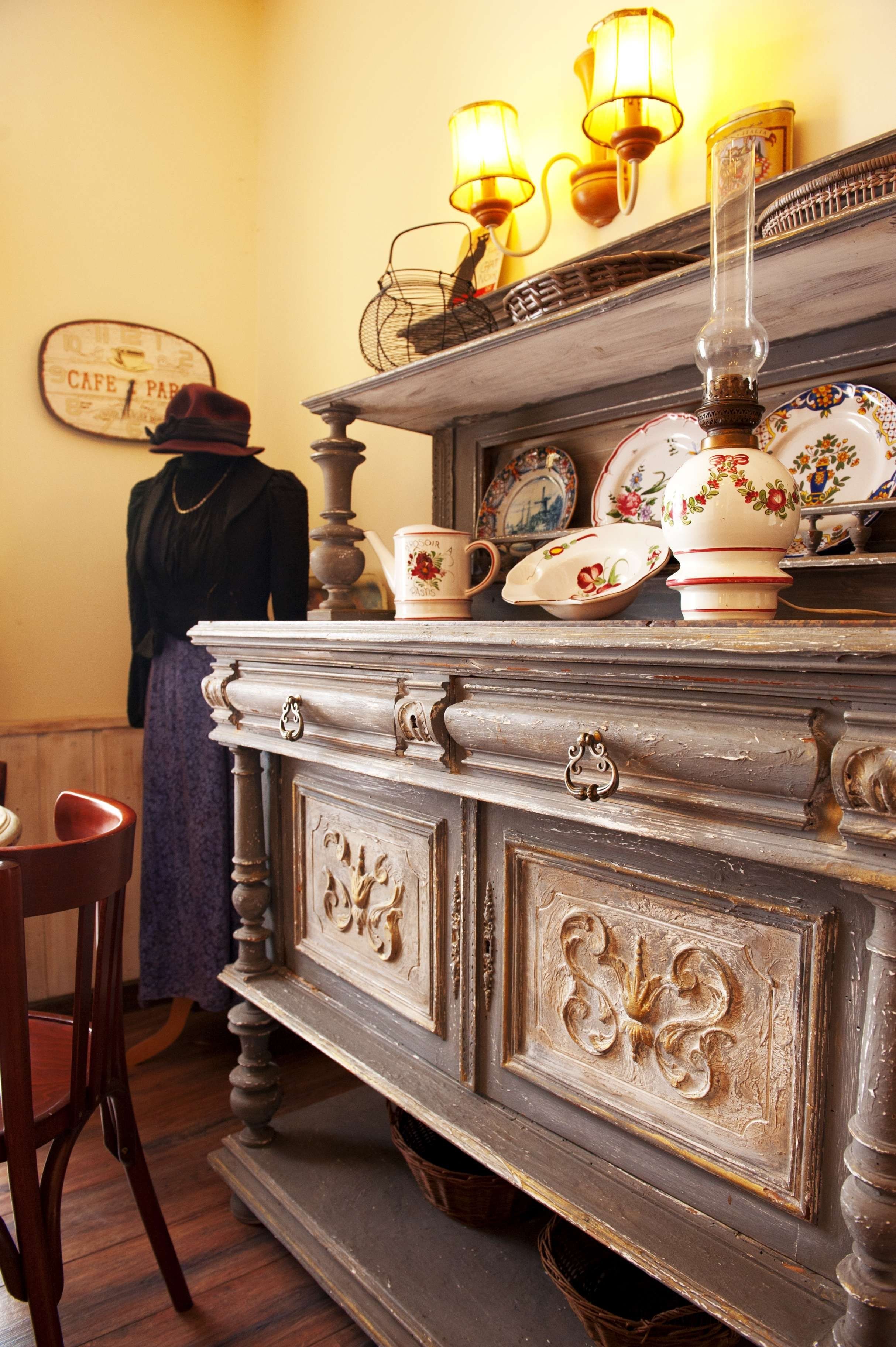 A vintage-style room with a wooden dresser, antique lamps, and a mannequin dressed in period clothing.
