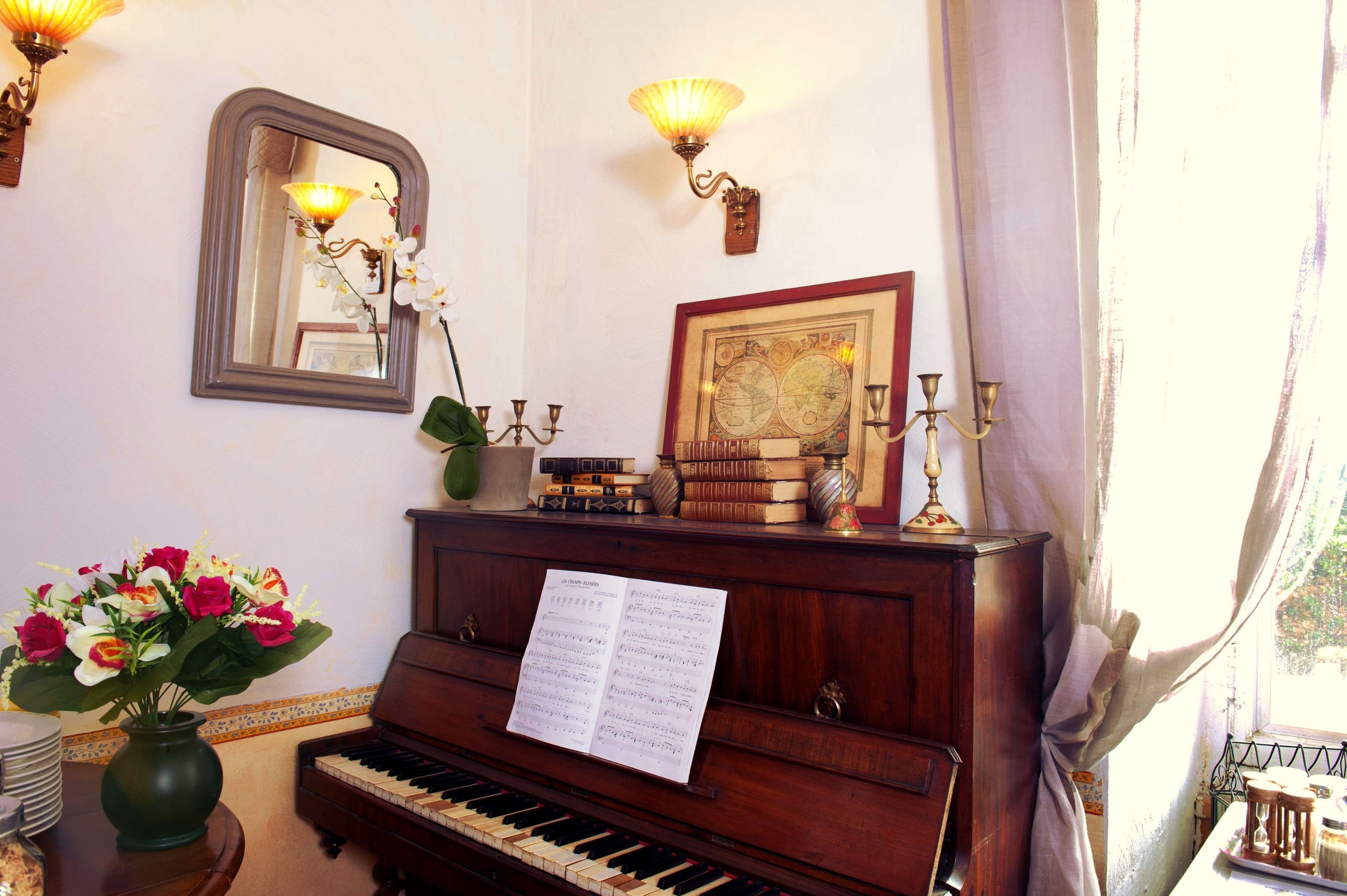 Un piano con partituras, un jarrón de flores, un mapa enmarcado y apliques decorativos en la pared.